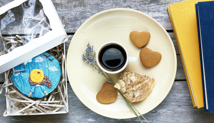 handmade painted image at gingerbread in a present box; coffee, heart shaped cookies, lavender, shell and books  are nearby on old wooden table