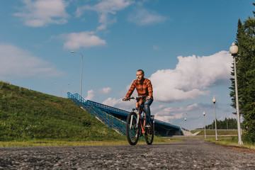 Plakat A man in jeans and a red shirt rides a bicycle on the road. The concept of an active lifestyle. Place for text.