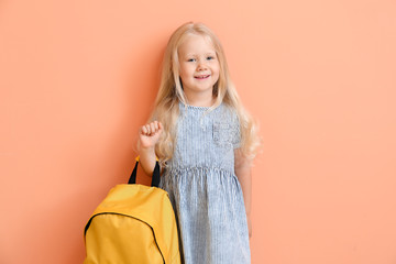 Cute little schoolgirl with backpack on color background