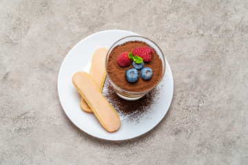 Classic tiramisu dessert with blueberries and raspberries and savoiardi cookies in a glass on concrete background