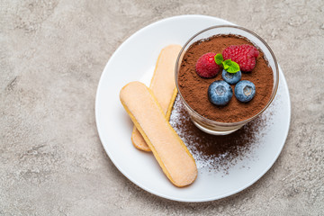 Classic tiramisu dessert with blueberries and raspberries and savoiardi cookies in a glass on concrete background