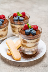 Classic tiramisu dessert with blueberries and raspberries and savoiardi cookies in a glass on concrete background