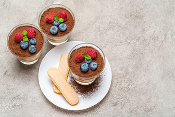 Classic tiramisu dessert with blueberries and raspberries and savoiardi cookies in a glass on concrete background