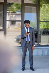 selective focus of african american businessman using smartphone while standing near office building