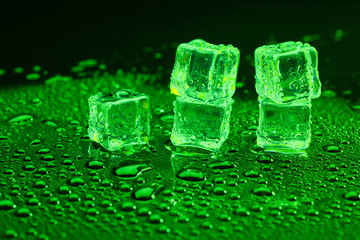Water drop with ice cubes on lighting green background.