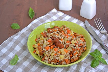 Pearl barley with chanterelles and vegetables in a green bowl on a dark brown concrete background. Recipes with seasonal chanterelle mushrooms. Cooking wild mushrooms.