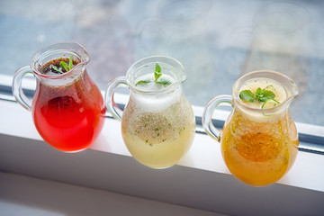 Three types of lemonade of different colors in glass decanters on the windowsill top view.