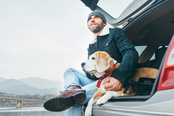 Man with beagle dog siting together in car trunk