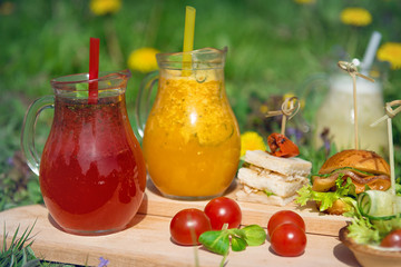Different types of lemonade in glass decanters during a picnic on a sunny day.
