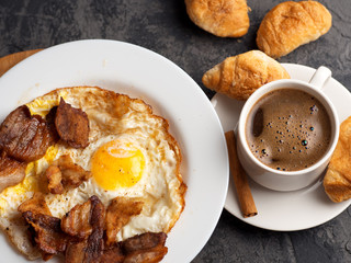 Scrambled eggs with slices of bacon for Breakfast and a Cup of espresso with croissants on the table