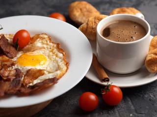 Omelet with slices of bacon and tomatoes in a white plate, a Cup of espresso with croissants. English breakfast