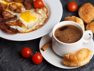 Omelet with slices of bacon and tomatoes in a white plate, a Cup of espresso with croissants. English breakfast