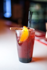 Close-up red cocktail with lemon and cinnamon stick on the bar, blurred background.