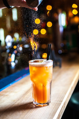 Close-up burning orange cocktail with lime on the bar, blurred background. Burning cocktail with sparks. Cocktail of fire