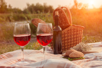 Romantic picnic at sunset. Picnic basket with red wine, bread