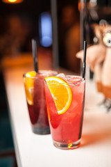 Close-up two orange cocktails with lemon on the bar, blurred background.