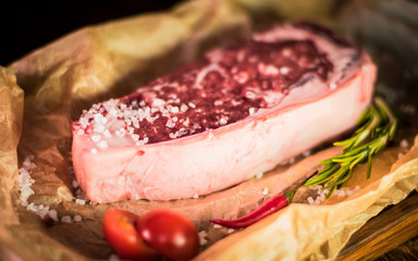 Marbled beef steak on parchment, coarse salt, cherry tomatoes, greens