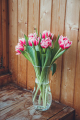 Bouquet of flowers in a vase on a wooden table by the window. Tulips in a vase by the window.