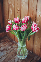 Bouquet of flowers in a vase on a wooden table by the window. Tulips in a vase by the window.