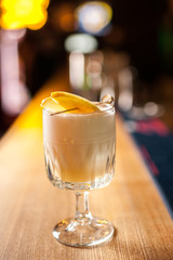 Close-up Pisco Sour cocktail with apple and cinnamon on the bar, blurred background.
