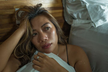 young beautiful sad and depressed Asian Indonesian woman in nightgown on bedroom floor by the bed feeling broken and lost suffering depression and anxiety