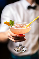 Bartender serving orange cocktail with orange and mint in bar