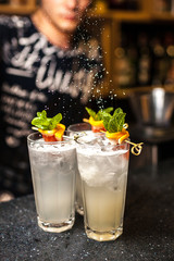 Bartender finishes preparation of alcoholic cocktail in crystal glass by adding a bitter of powdered sugar. Close-up of expert bartender making cocktails in bar.