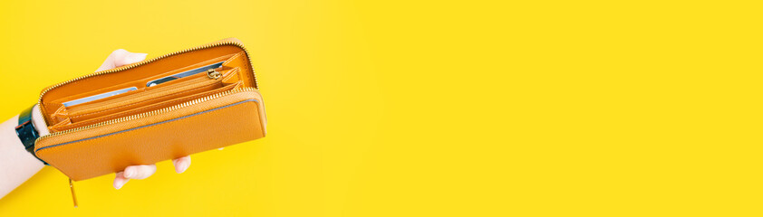 web banner design for woman fashion in spring and summer concept with beauty woman hand hold and open modern brown leather purse or wallet in left hand with yellow pastel background