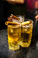 Three orange cocktails with a cinnamon stick in a dark bar