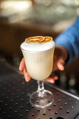 Close up Pisco Sour cocktail with dried orange on bar