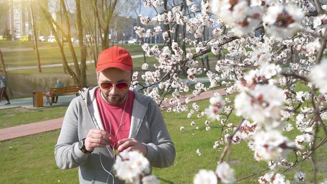 Funny drunken man with smartphone listens to music and dances in city park