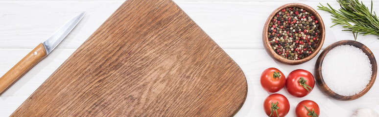 panoramic shot of wooden chopping board, cherry tomatoes, knife, salt, spices and rosemary