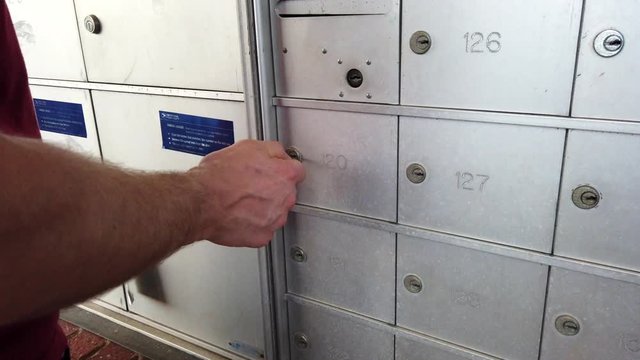 a Caucasian man taking mail from a letterbox at a community apartment post station in slow motion.