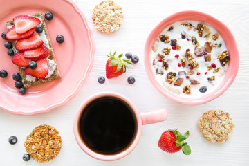 Yogurt for breakfast with granola, berries and strawberry. A cup of black coffee, top view. Bright colors. Tasty healthy snack. 
