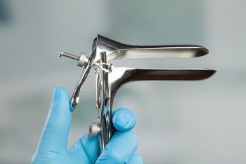 doctor's hand in medical gloves holds a adjustable medical speculum