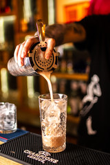 Close-up of expert bartender making cocktail on the bar, blurred background.