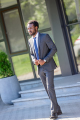 handsome african american businessman looking away while standing near office building