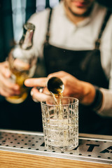 Close-up of expert bartender making cocktail on the bar, blurred background.