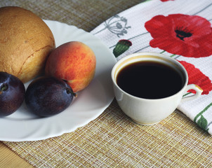 Homemade breakfast, cup of coffee, bun and fruit on a plate, peach and plums, white napkin with red poppies