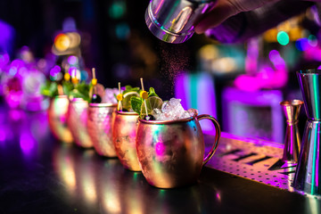Bartender finishes preparation of cocktails in metal cup by adding a bitter of cinnamon. Close-up of expert bartender making cocktail in bar.