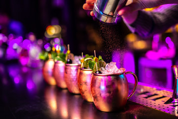 Bartender finishes preparation of cocktails in metal cup by adding a bitter of cinnamon. Close-up...