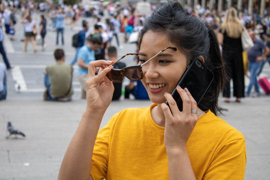 giovane asiatica sorridente mentre parla al telefono in pubblico