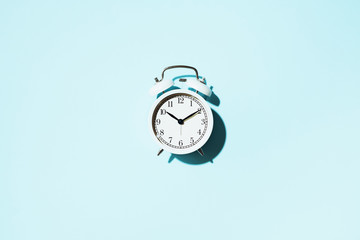 White alarm clock with hard shadow on blue background. Top view