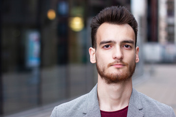 Fototapeta premium Close up portrait of a serious European brunet formal dressed businessman with a beard standing outdoor and looking at camera in a jacket. Confident young business person.