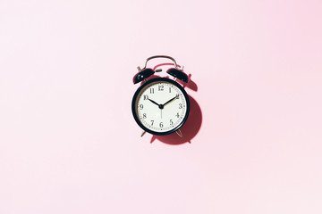 Black alarm clock with hard shadow on pink background. Top view