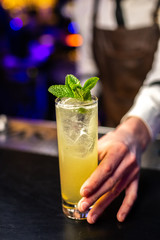 Close-up of expert bartender serves cocktail on the bar, blurred background.