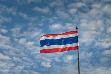 Thai national flag is waving by turbulent or severe wind direction, with background of blue cloudy sky.