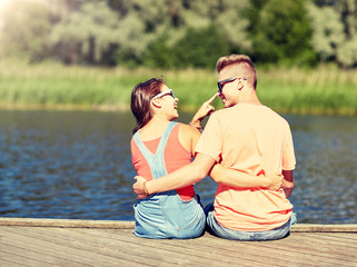 vacation, love and people concept - happy teenage couple sitting and hugging on river berth at summer