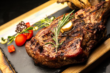 Grilled Tomahawk steak ribeye with rosemary, butter and cherry tomatoes on wooden plate