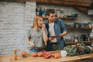 Trendy couple peeling and cutting vegetables from the market in rustic kitchen
